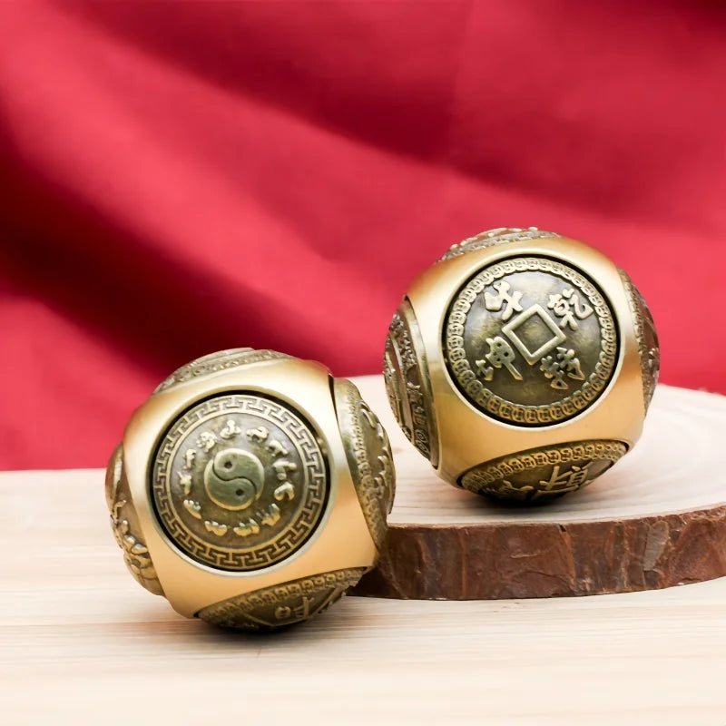 A pair of golden Chinese lucky coin fidget toys resting on a wooden surface with a red fabric background.