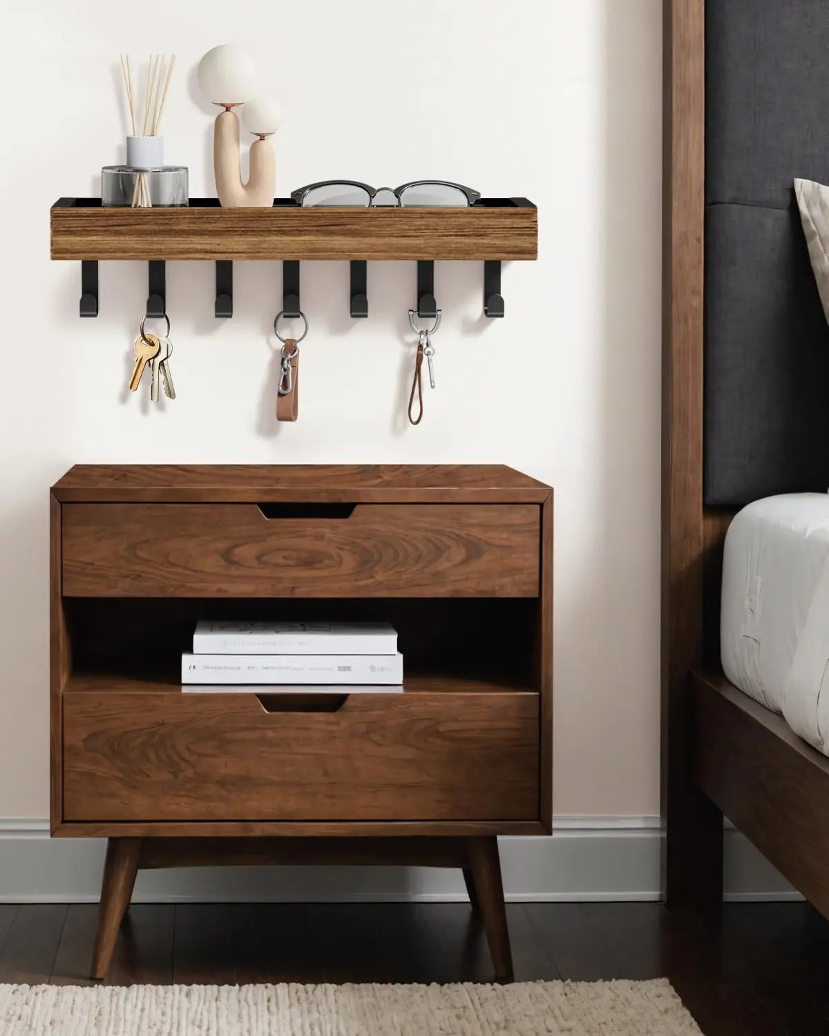 A rustic wooden floating shelf with hooks mounted on a wall above a dark wood storage box.