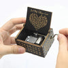 An antique engraved wooden music box with a lid showing text and a winding key is held in a hand.
