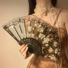 A close-up of an elegant black and white lace rose folding fan being held against a person's chest.