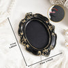 A black vintage baroque resin hanging photo frame with gold accents shown on a white surface.