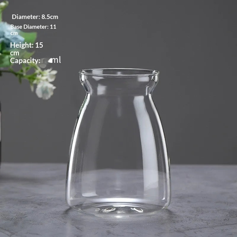 A clear glass vase with a wide mouth and narrow neck, shown on a gray surface.