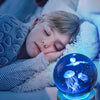 A young girl rests her head on a white fluffy blanket next to a blue crystal ball night light featuring glowing jellyfish.