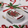 A white plate with a red and green poinsettia rectangle napkin set on a festive holiday tablecloth.