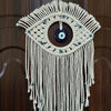Macrame wall hanging featuring a woven eye design with blue glass beads and fringe.