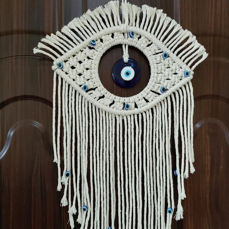 Macrame wall hanging featuring a woven eye design with blue glass beads and fringe.