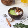 A dark brown coconut shell serving bowl filled with light colored fruit and nuts on a white surface.