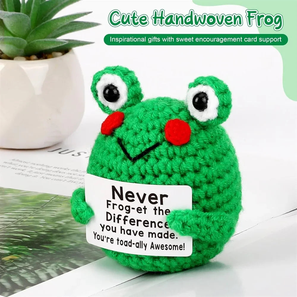 A handmade green crochet frog ornament with red accents sitting on a white background.