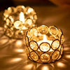 A close-up of a golden crystal tealight candle lantern holder casting warm light and shadows.