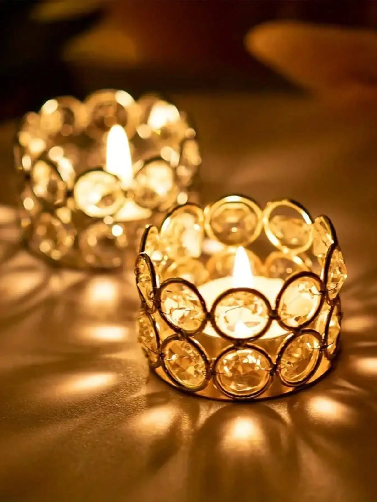 A close-up of a golden crystal tealight candle lantern holder casting warm light and shadows.