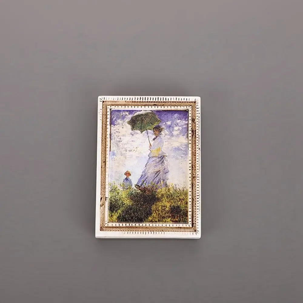 A framed painting featuring a woman under an umbrella in a field, displayed as a fridge magnet.