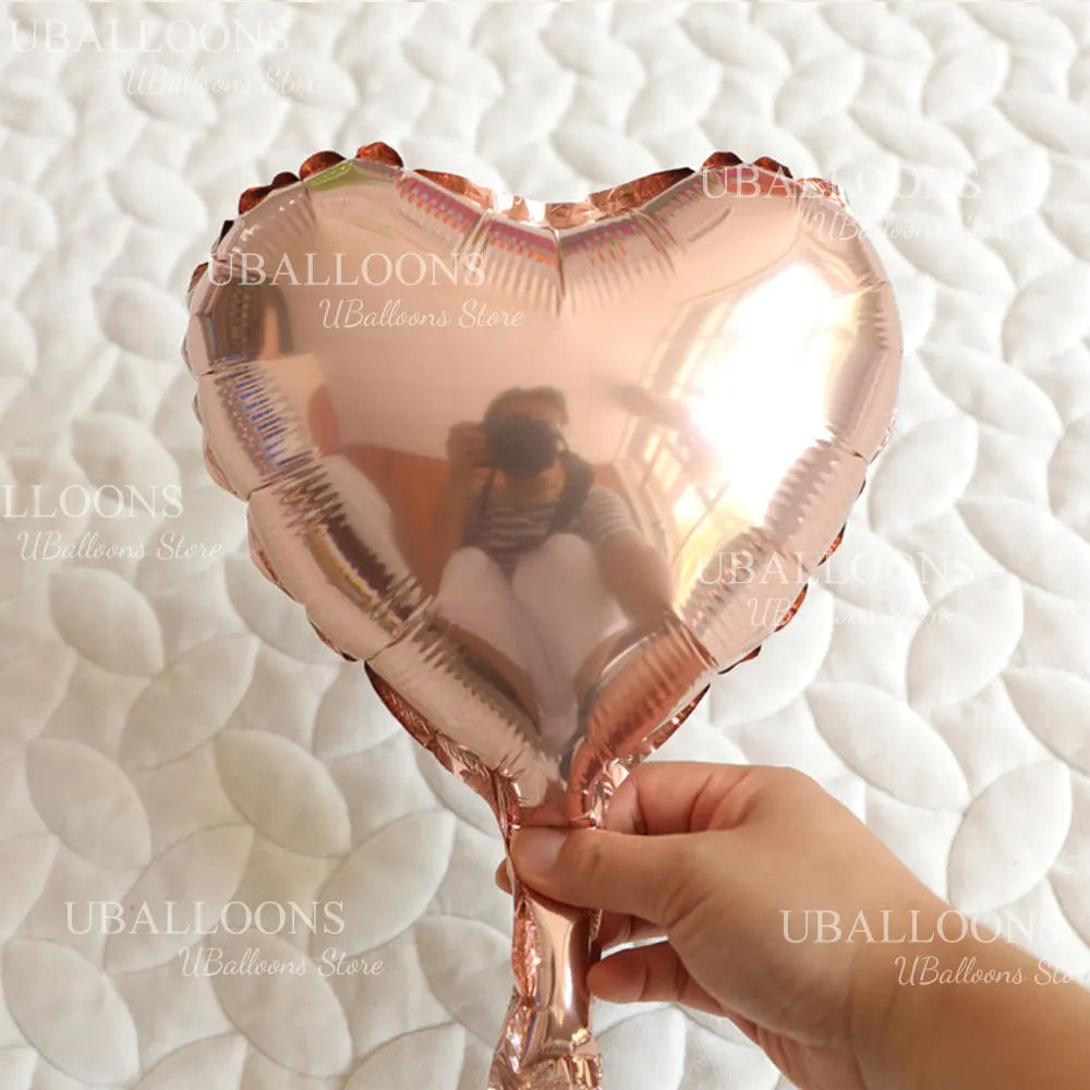 A hand holds a pink heart-shaped foil balloon for celebrations.