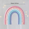 A rainbow-shaped cake topper made of pink and blue fondant or gum paste, measuring about 8.5cm.