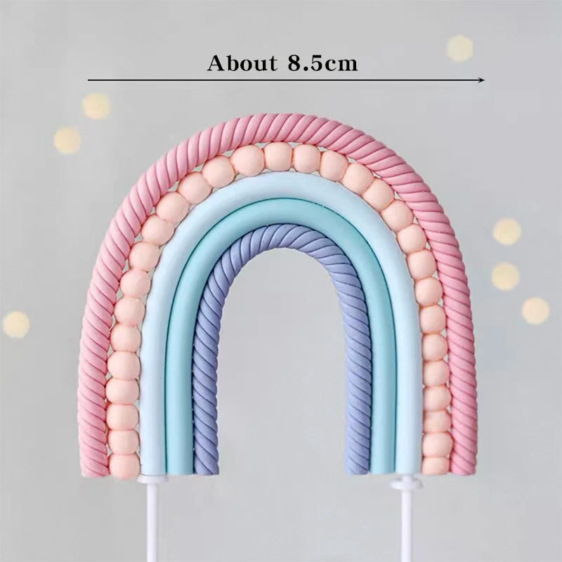 A rainbow-shaped cake topper made of pink and blue fondant or gum paste, measuring about 8.5cm.