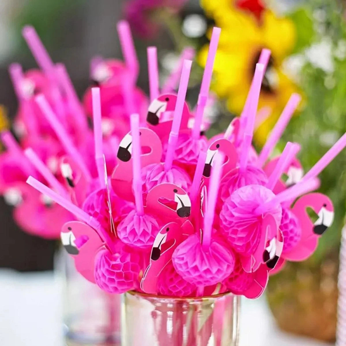 A bouquet of bright pink 3D flamingo and pineapple paper straws in a glass container.