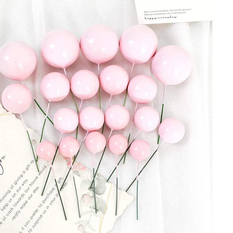 A set of twenty pink balloon cake toppers on thin green sticks with a handwritten message.