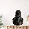 A black resin statue of an alien duck with intricate, textured scales sitting on a wooden surface.