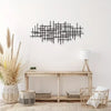 Black geometric metal wall art sculpture mounted on a white wall above a light wood console table.