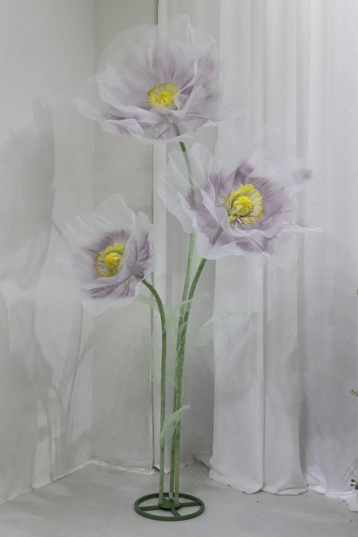 A large artificial silk purple and white poppy flower displayed on a green stand.