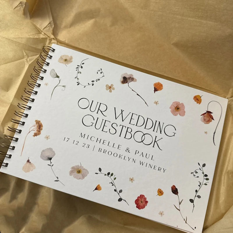 A white spiral-bound guestbook titled Our Wedding Guestbook featuring floral illustrations and names Michelle & Paul.