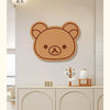 A round, brown cartoon bear face felt wall decor panel mounted on a white wall above a light wood cabinet.