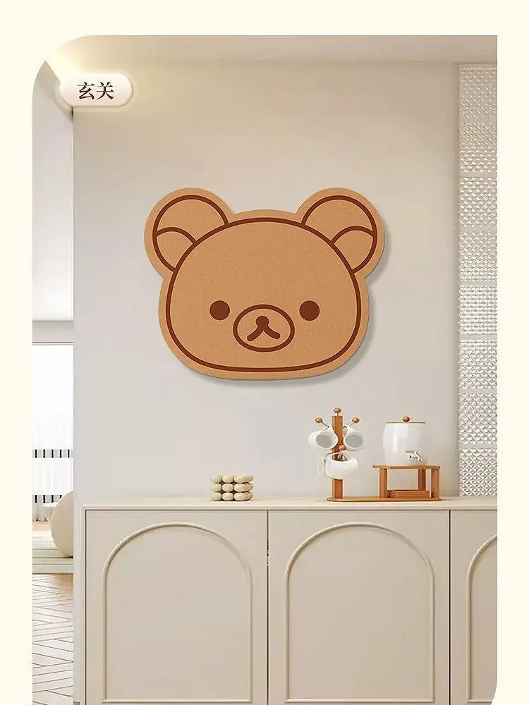 A round, brown cartoon bear face felt wall decor panel mounted on a white wall above a light wood cabinet.