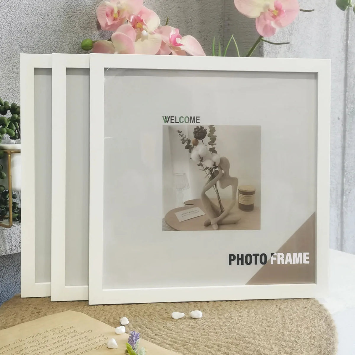 A set of three white wooden photo frames displayed on a light-colored surface with pink flowers in the background.