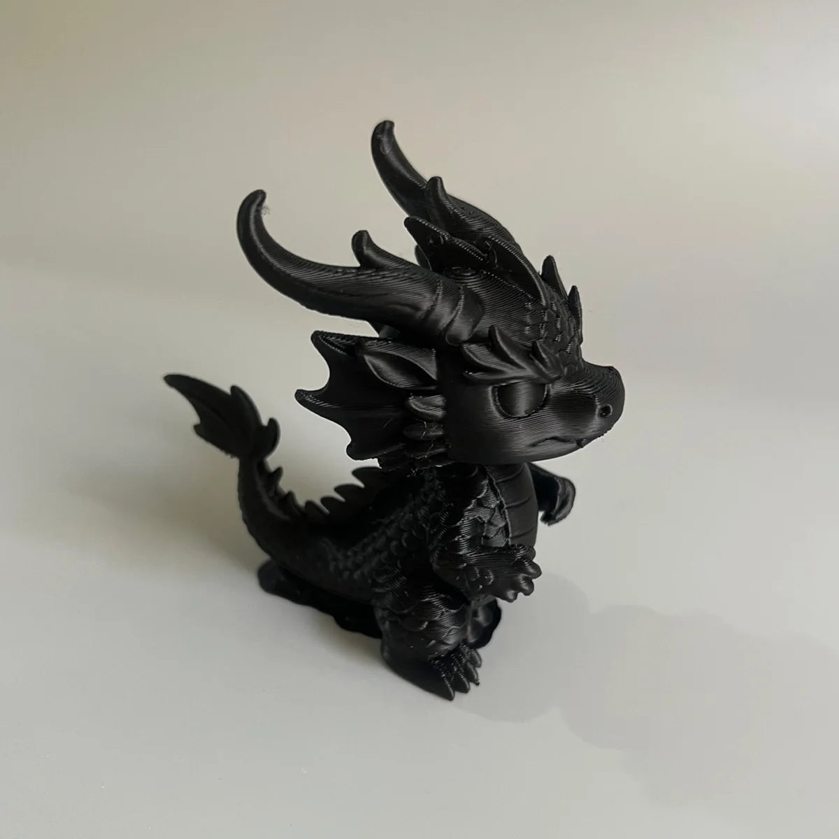 Figurine de dragon miniature noir pour bureau avec des cornes pointues et des traits faciaux féroces.
