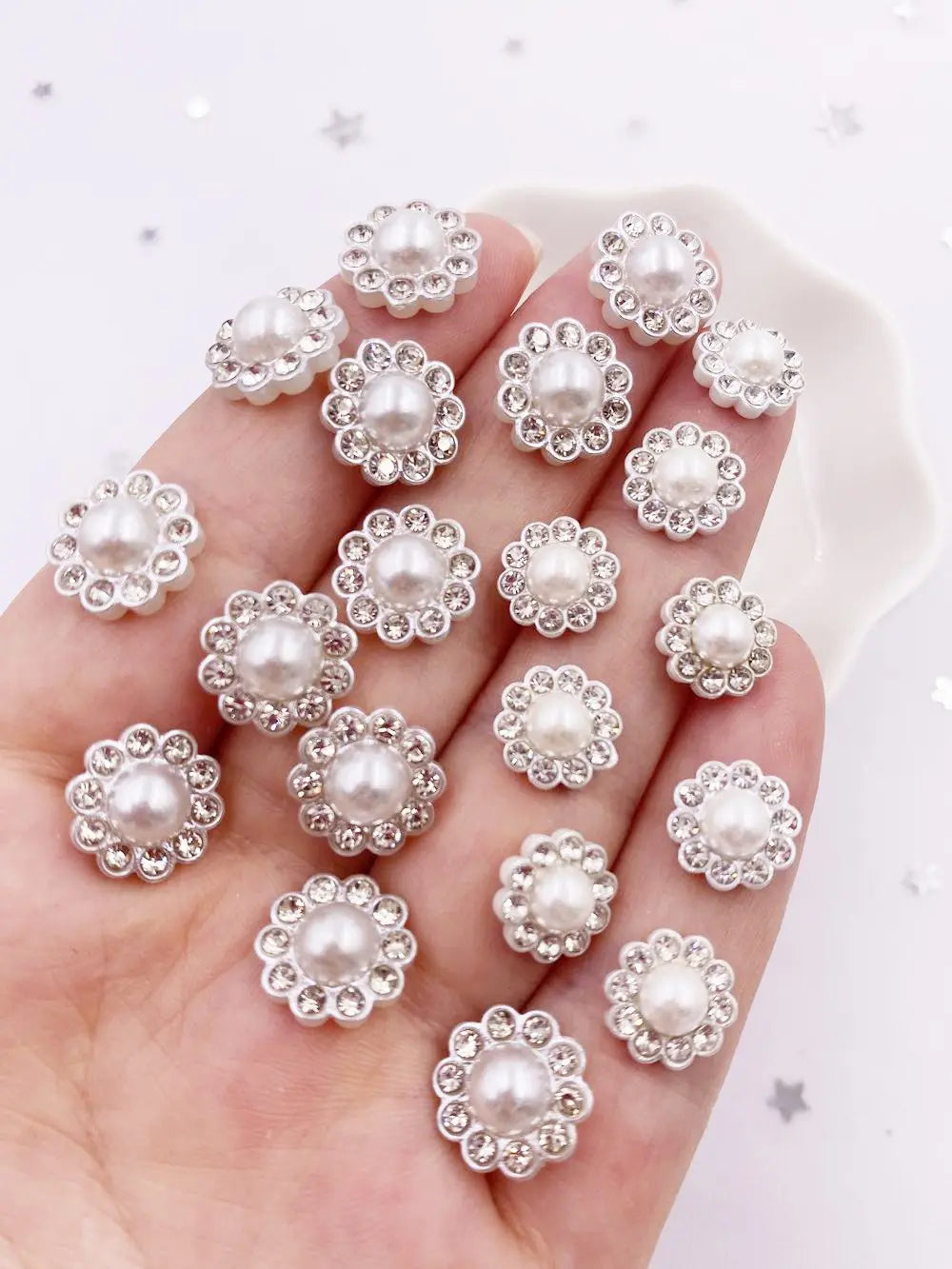 A hand holds a collection of 50 pearl rhinestone flatback crystals for DIY crafts and decor.