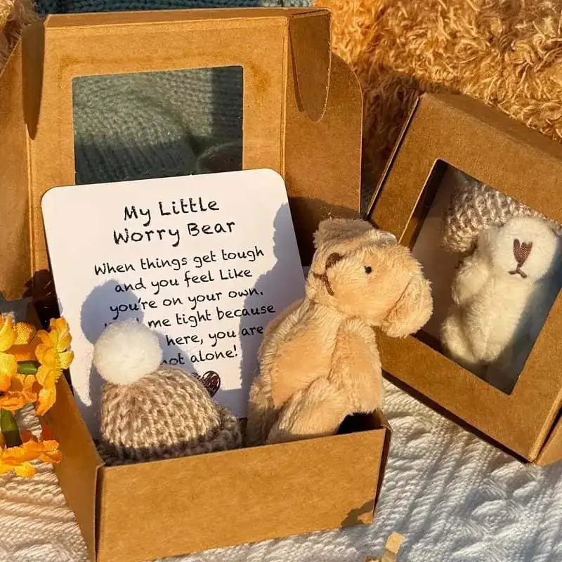 A small tan plush bear is displayed in a cardboard box with an encouraging card.