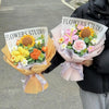 A bouquet of handmade crochet flowers in pink and yellow hues wrapped in tissue paper.
