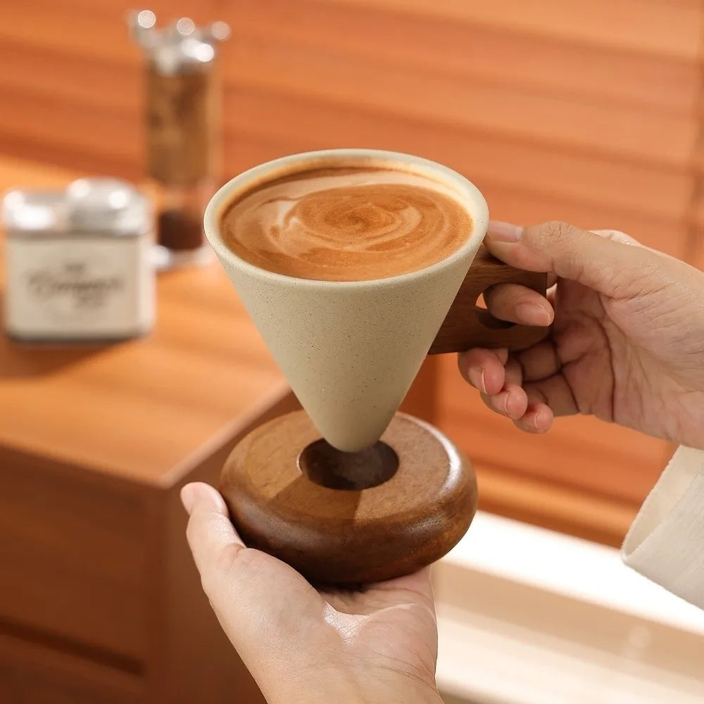 A hand holds a ceramic coffee mug with latte art on a wooden base.