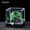 A clear glass box containing a vibrant green and black natural crystal rough stone specimen.