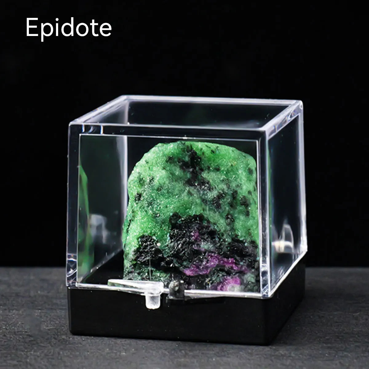 A clear glass box containing a vibrant green and black natural crystal rough stone specimen.