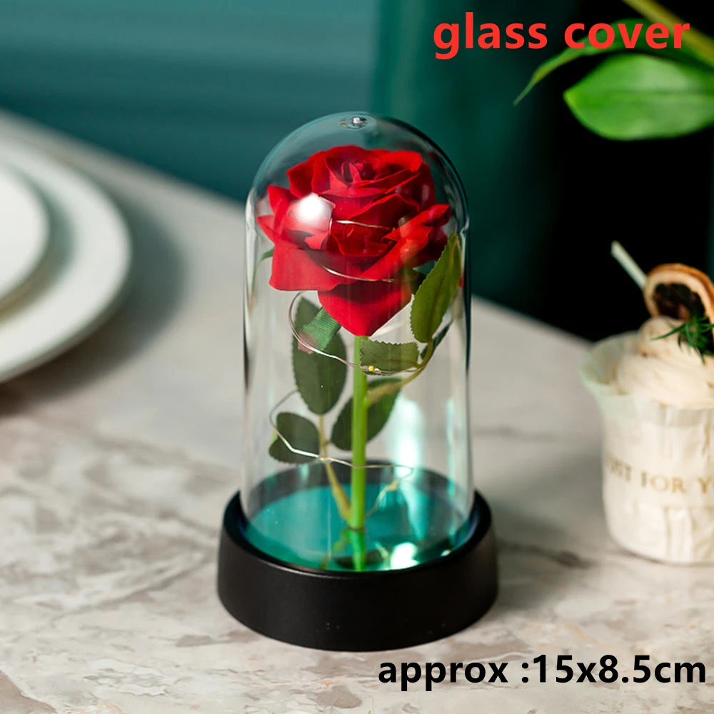 A red rose in a glass dome sits on a black base, displayed on a white surface.