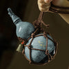 A dark gray ceramic wine gourd with a stopper and a woven brown cord, suspended by a hand.