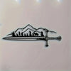 Black silhouette of a mountain landscape with figures and a sword on a metal wall art design.