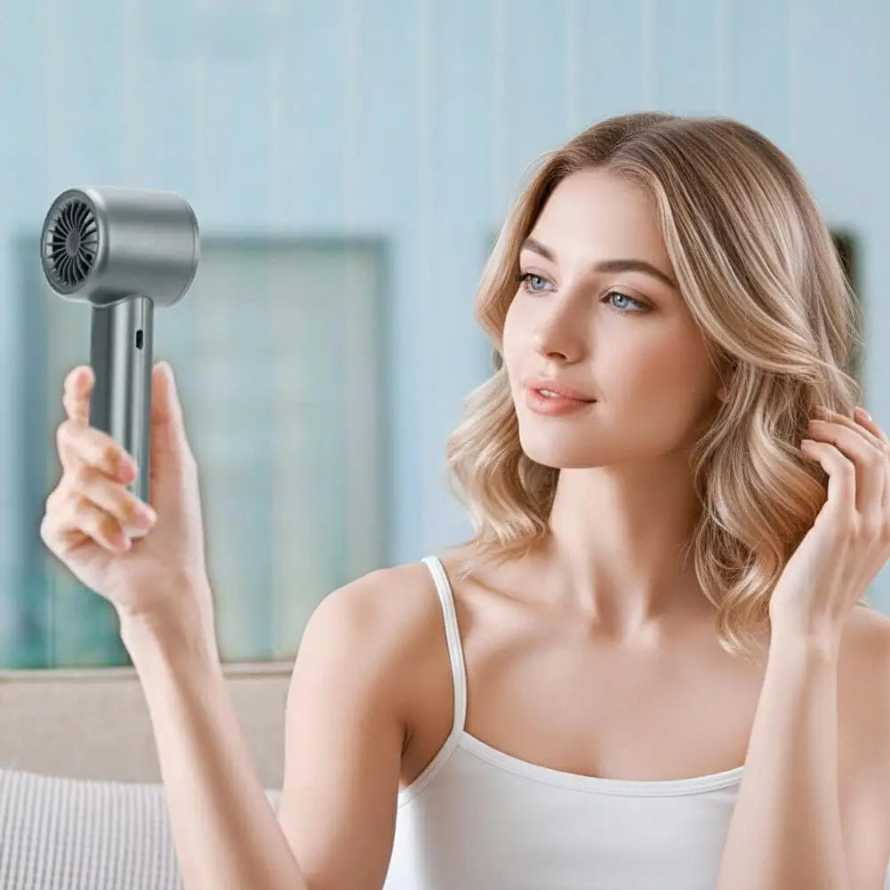 A woman is using a portable handheld fan with a silver finish to cool her face.