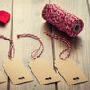 A roll of red and white cotton twine next to several small tags on a wooden surface.