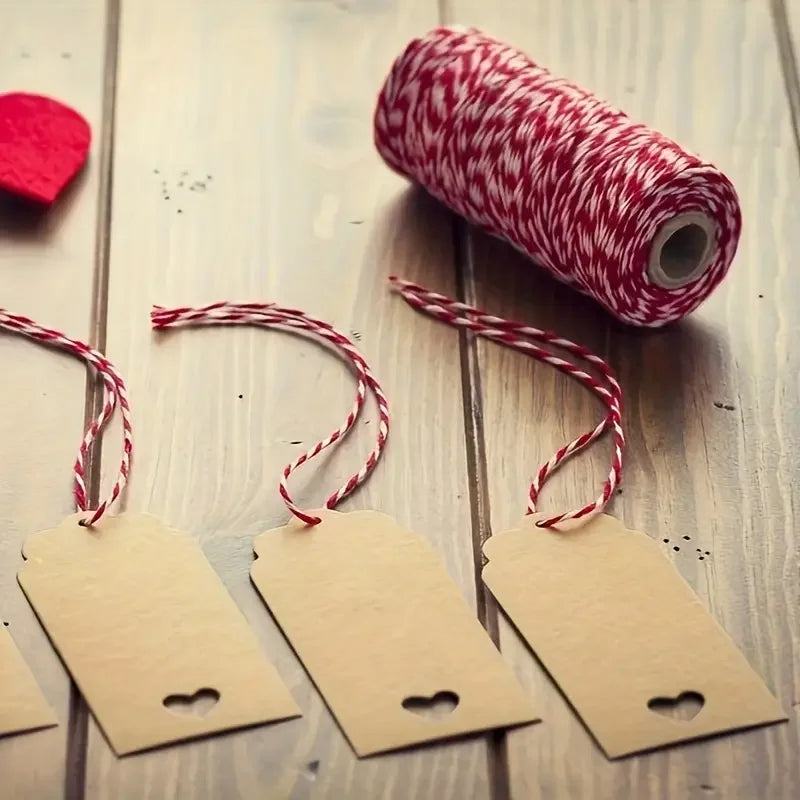 A roll of red and white cotton twine next to several small tags on a wooden surface.
