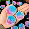 Hand holding iridescent blue and pink agate crystal geodes on a dark surface