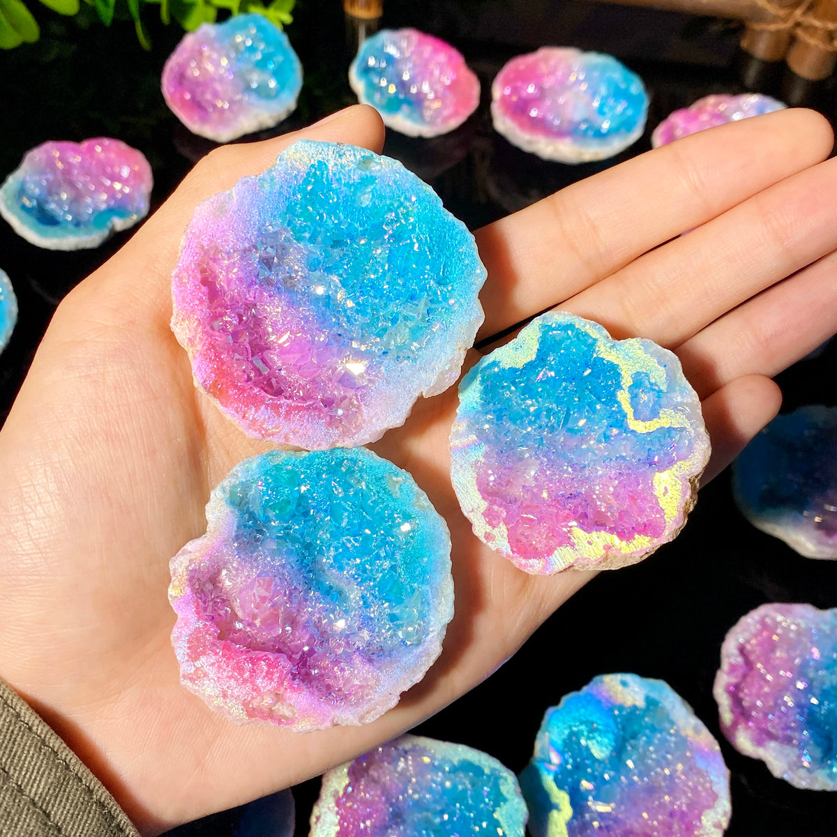 Hand holding iridescent blue and pink agate crystal geodes on a dark surface