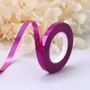 A roll of vibrant purple glitter satin ribbon is shown against a background of white flowers.