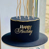 A dark navy blue birthday cake with gold lettering and thin acrylic toppers on a black cake board.