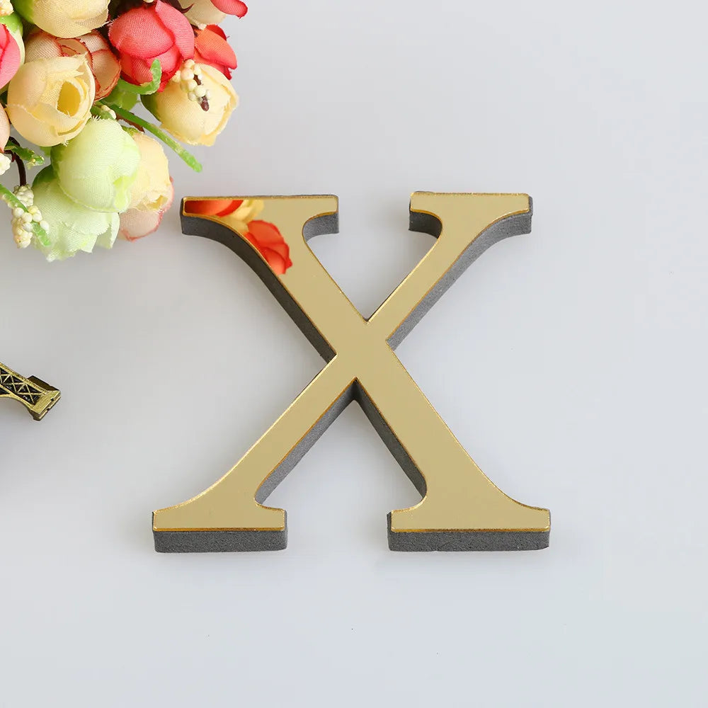 A gold letter X cutout with a textured gray base, placed next to a bouquet of pink and yellow flowers.
