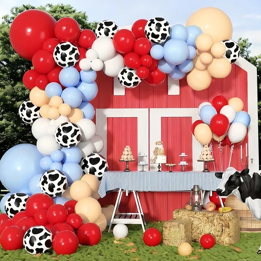 A red barn decorated with a balloon garland featuring various colored balloons and black and white polka dot balloons.