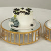 A white cake topped with dark berries and greenery displayed on a gold-rimmed glass cake stand.