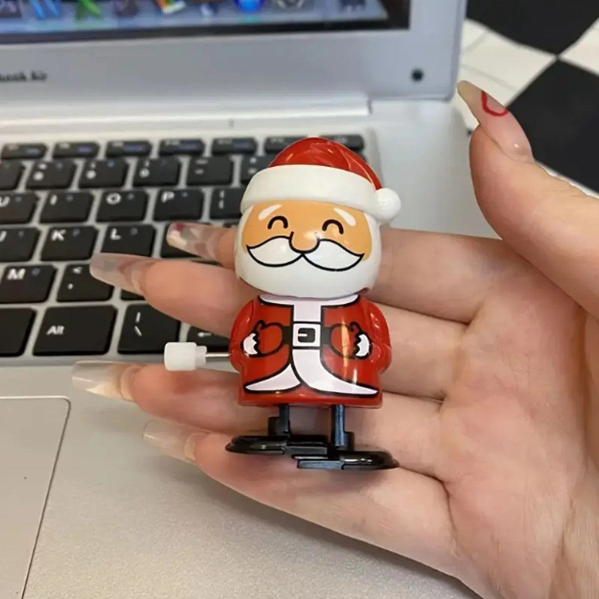 A hand holds a small clockwork wind-up figurine of a man with a white beard and a Santa hat.