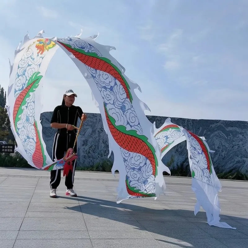 Una persona con atuendo negro realiza una danza de dragón con grandes accesorios de tela blanca con diseños rojos y verdes.