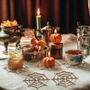 A still life featuring wooden spider web ornaments, a lit candle, and a cup of coffee on a white tablecloth.